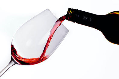 Red wine being poured from a bottle into a tilted wine glass against a white background.