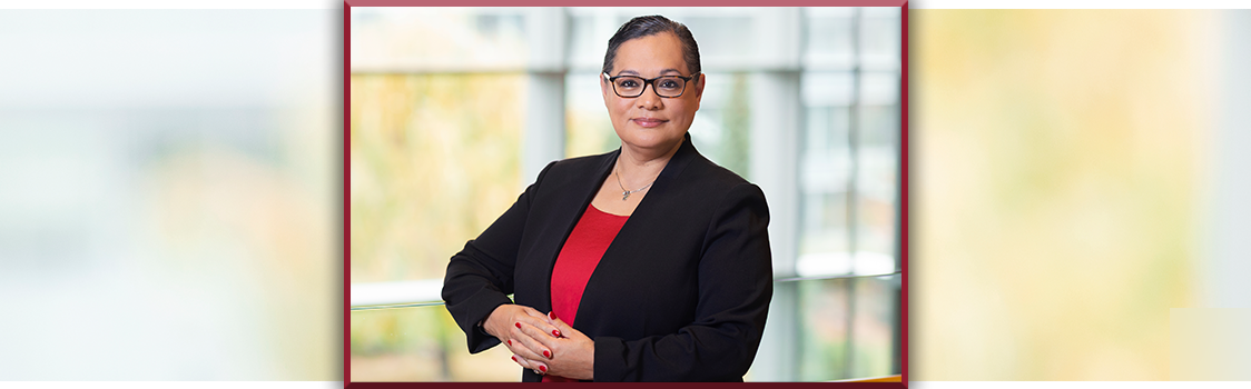 Spokane Judge Gloria Ochoa‑Bruck stands indoors in a black blazer and red top, hands folded, with soft natural light behind them.