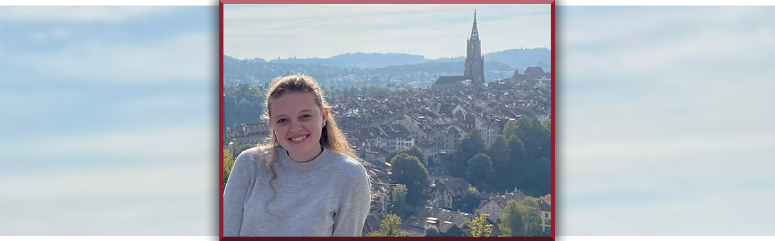 Nicole Dalton stands overlooking a European cityscape with clustered rooftops and a tall church tower rising in the distance.