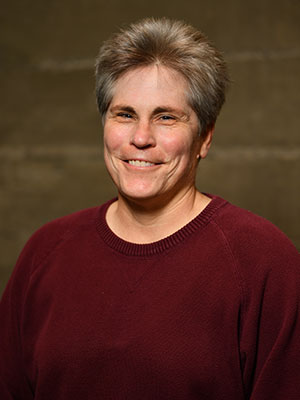 Tiffany Reiss wearing a maroon sweater, posed against a muted brown studio background.