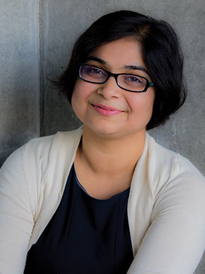 Amrita Lahiri seated against a concrete wall wearing a dark top and a light cardigan.