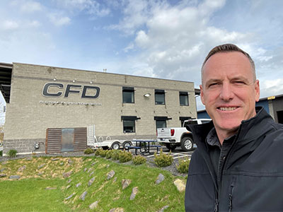 Bob Wiese standing outside the Custom Fabrication Design building, with the CFD logo visible on the gray exterior.