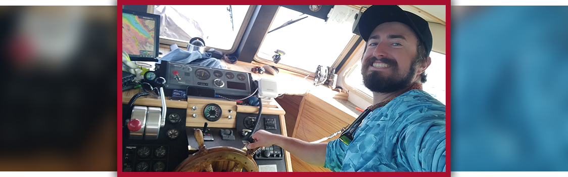 Sean Russell at the helm of a boat, steering near the instrument panel and windows of the cabin.
