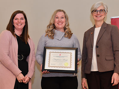 Stephanie Rink standing at center holding her award certificate, with Anna McLeod on the left and WSU Provost Elizabeth Chilton on the right.