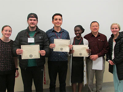 Sophia Sullivan-Pollard, Johnathan Lyga, Chris Ayala, Felicia Adesope, Professor Bernie Wong-on-Wing, and Anna-Maria Rehwaldt standing together with award certificates.