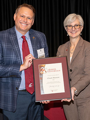 Chuck Munson and Chancellor Elizabeth Chilton stand together holding a framed service award during a recognition event.