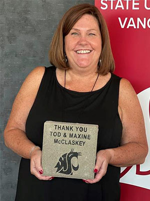 Jenni Sandstrom holding a stone plaque engraved with “Thank you Tod & Maxine McClaskey” and the WSU cougar logo, standing before a WSU Vancouver backdrop.