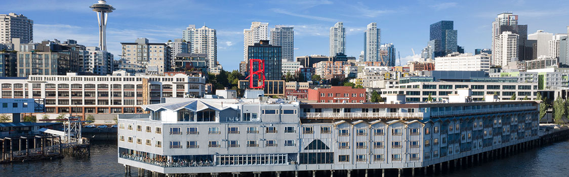 View of the Edgewater Hotel on Pier 67 extending over the water, with Seattle’s skyline and the Space Needle rising in the background.