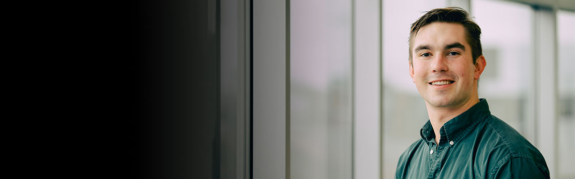 Brian Patrick stands indoors near tall windows, wearing a dark green button‑down shirt with soft natural light illuminating the space.