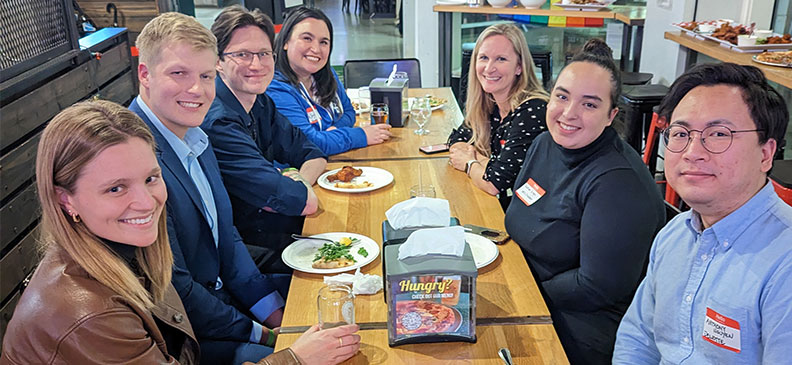 Students and alumni sit together at a long table inside Flatstick Pub, sharing food and conversation.