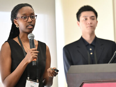 Aline Uwase speaks into a microphone while Junhui Zhang stands beside her at a podium as the U‑Shield app founders present their work.