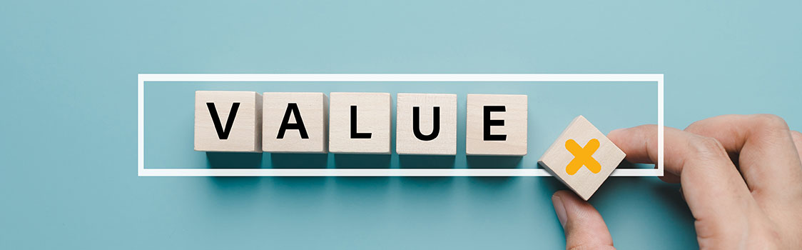 Wooden blocks spelling VALUE on a blue background, with a hand placing an additional block marked with a yellow X inside a white rectangular outline.