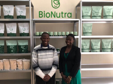 Jofrey Raymond and Christina Charles stand in front of shelves stocked with BioNutra products, posed beneath the company’s green logo.