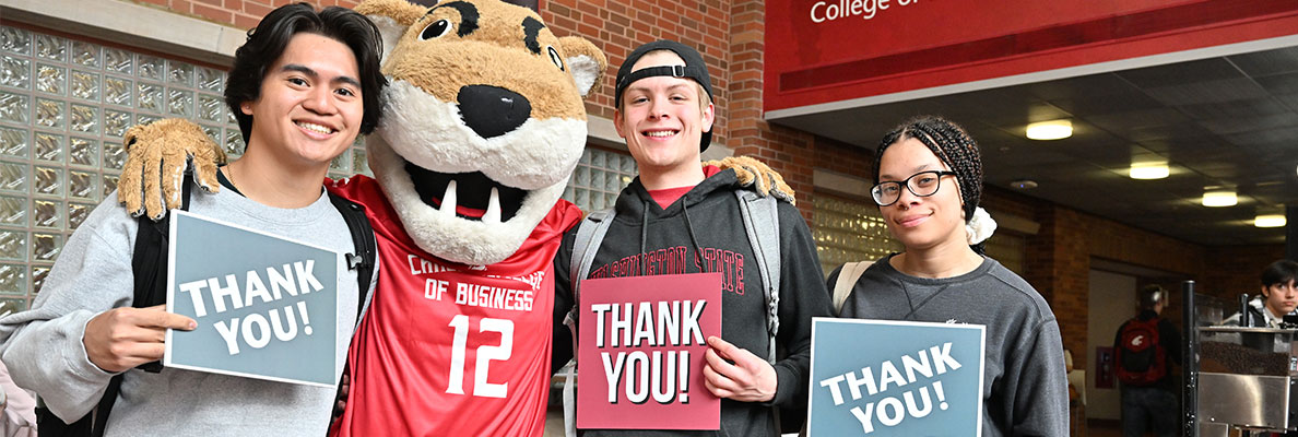 Students stand with the WSU mascot, Butch, each holding a sign that reads “THANK YOU!” in front of a College of Business building.