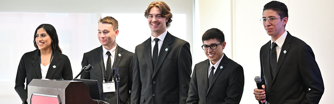 Central Solutions Group team members stand together in suits at a podium as one member speaks into a microphone, presenting their concept for non‑emergency medical transportation.