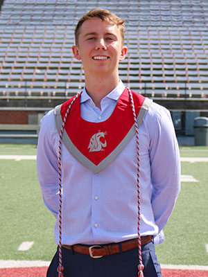 Christian Wilgis stands on a football field wearing a WSU graduation stole and honor cords.