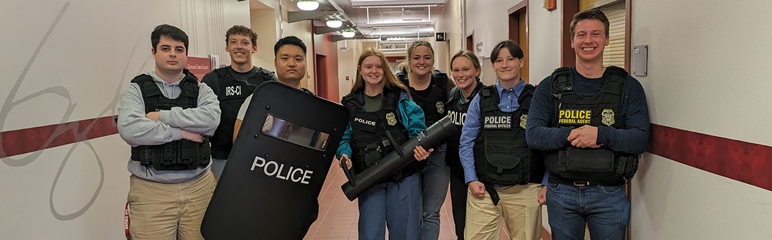 Carson accounting students wearing “POLICE” jackets walk through a hallway with IRS Criminal Investigation special agents while conducting a mock fraud investigation.