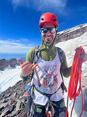 Ian Cox stands on a snowy mountain slope in climbing gear, holding a rope during a mountaineering trek.
