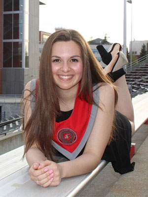 Megan Fisher wearing a graduation stole poses on stadium bleachers, lying on her stomach with legs raised behind her