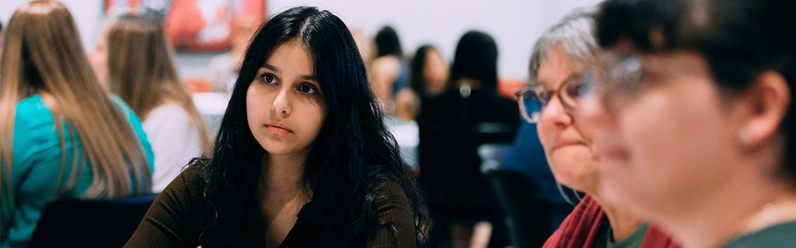 Participants at the Women in Business event sit together in conversation, with groups gathered in the background discussing networking, educational, and professional opportunities.
