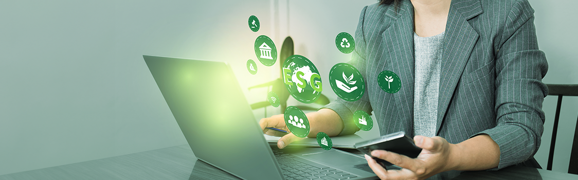 Person in a gray blazer working on a laptop while holding a smartphone, surrounded by glowing green ESG icons representing sustainability and governance.