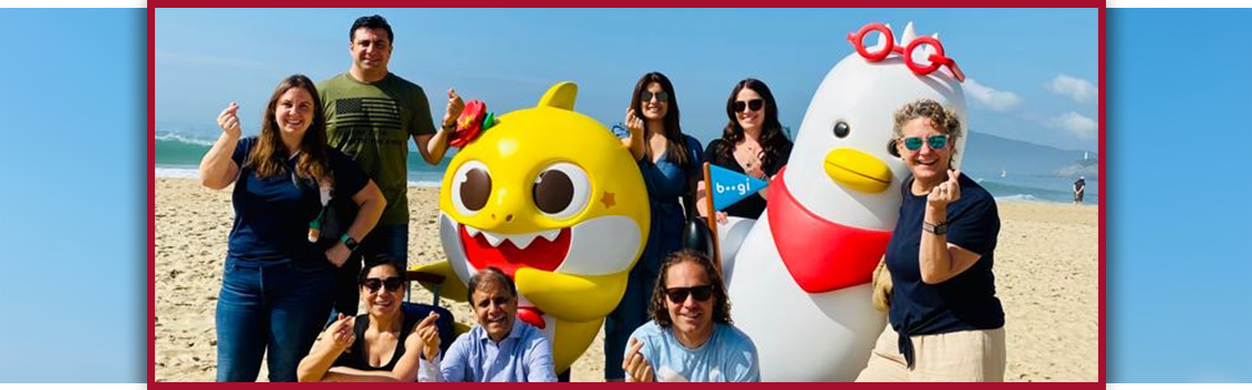 Julie Nelsen and colleagues making the “finger heart” gesture on a sunny South Korean beach beside large yellow and white character statues.
