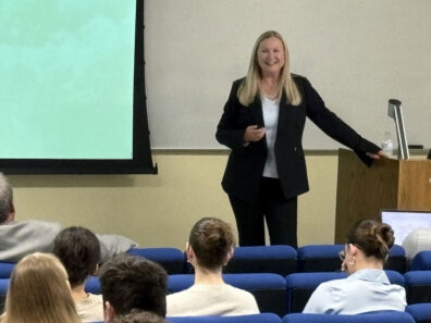 Carrie Cheshier speaks to business students during the fall 2024 Walton Lecture, standing at the front of a classroom near a podium and projection screen.