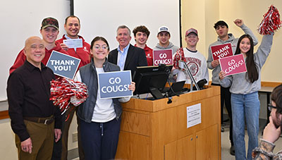 Carson College of Business students gathered around a podium holding “Go Cougs!” and “Thank You!” signs and red pom-poms while celebrating their top-performing portfolio in the D.A. Davidson Systematic Investment Plan Competition.