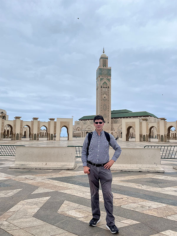 Alberto Sa Vinhas stands in the courtyard of the Hassan II Mosque in Casablanca, Morocco, with the mosque’s tall minaret rising behind them.