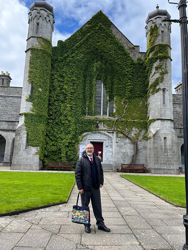 Kunter Gunasti stands in the Quadrangle at the University of Galway before an ivy‑covered stone building with arched walkways and manicured lawns.