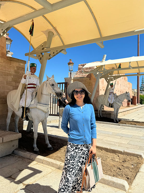Li Xu stands at the Mausoleum of Mohammed V in Rabat, Morocco, with ceremonial guards on white horses positioned under a shaded archway behind them.