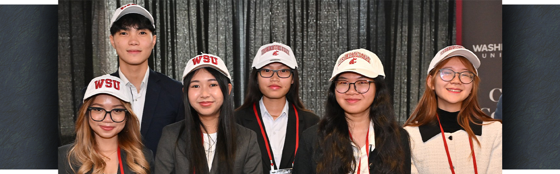 Six individuals from Cambodian CamEd Business School, representing student-led venture teams 'Mango Glow' and 'Ompovision,' wearing business attire and WSU caps, standing in front of a black curtain with name tags and lanyards.
