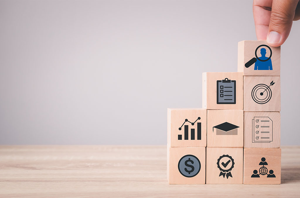 Hand placing a wooden block with icons representing goals, teamwork, and achievement.