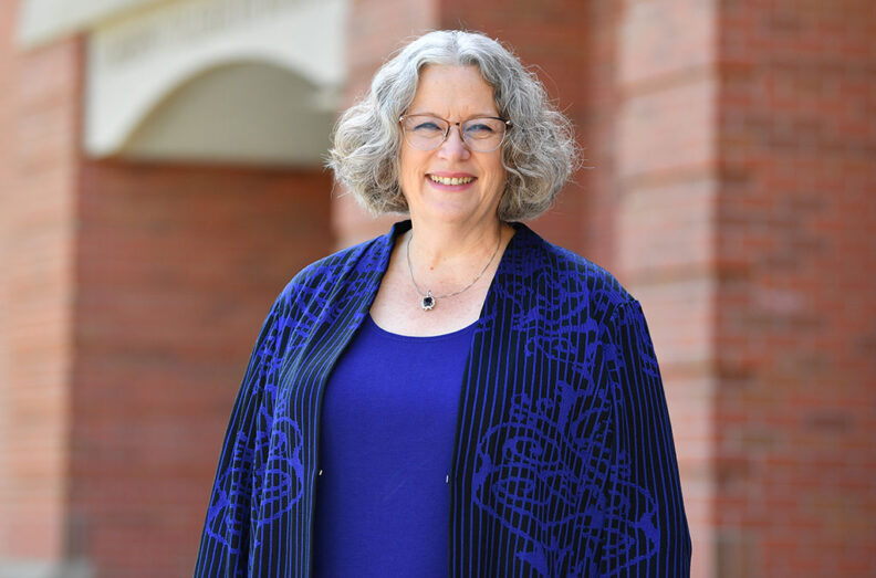 Carson College of Business Dean Debbie Compeau standing outside a brick building, wearing a blue top and patterned jacket.