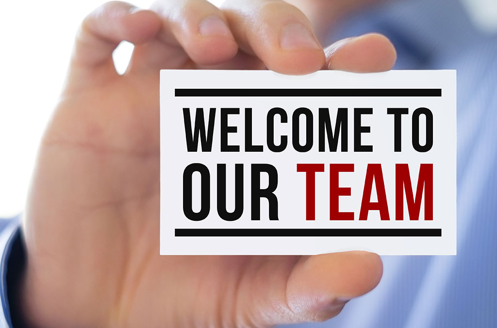 Hand holding a card that reads “Welcome to our team” in bold black and red lettering.