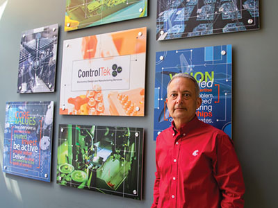 Andy LaFrazia standing in front of a wall display featuring colorful ControlTek-themed graphics and signage, wearing a red WSU shirt.