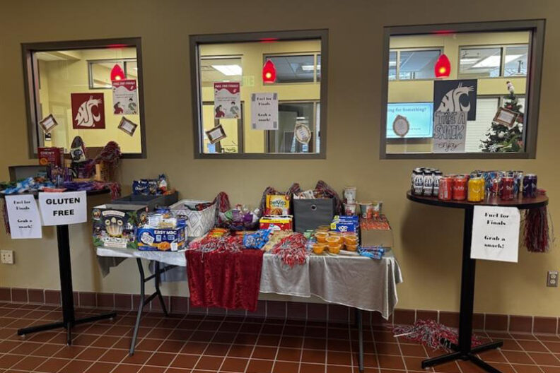 Fuel for Finals food drive display with tables stocked with snacks, drinks, and pantry items, arranged under windows with WSU‑themed signs and decorations.