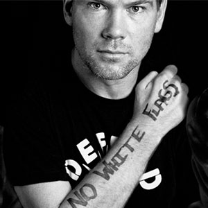 Steve Gleason’s arm shown in black and white with the handwritten message “NO WHITE FLAGS” visible, wearing a shirt with partially visible bold lettering.