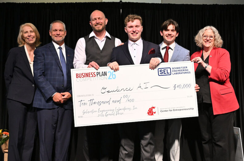 Opulence AI team members hold a $10,000 grand prize check on stage at the 2026 Business Plan Competition.