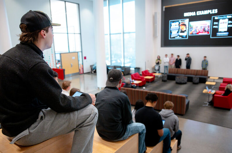 Students watch as teams present startup ideas and app concepts in a large classroom during an entrepreneurship pitch event.