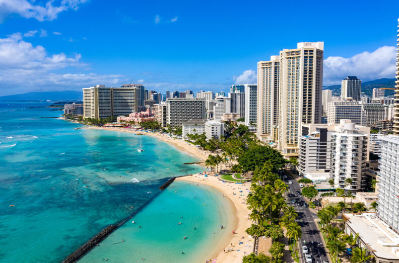Aerial view of Waikiki in Honolulu, Hawaii, with high-rise hotels lining a turquoise coastline and sandy beaches.