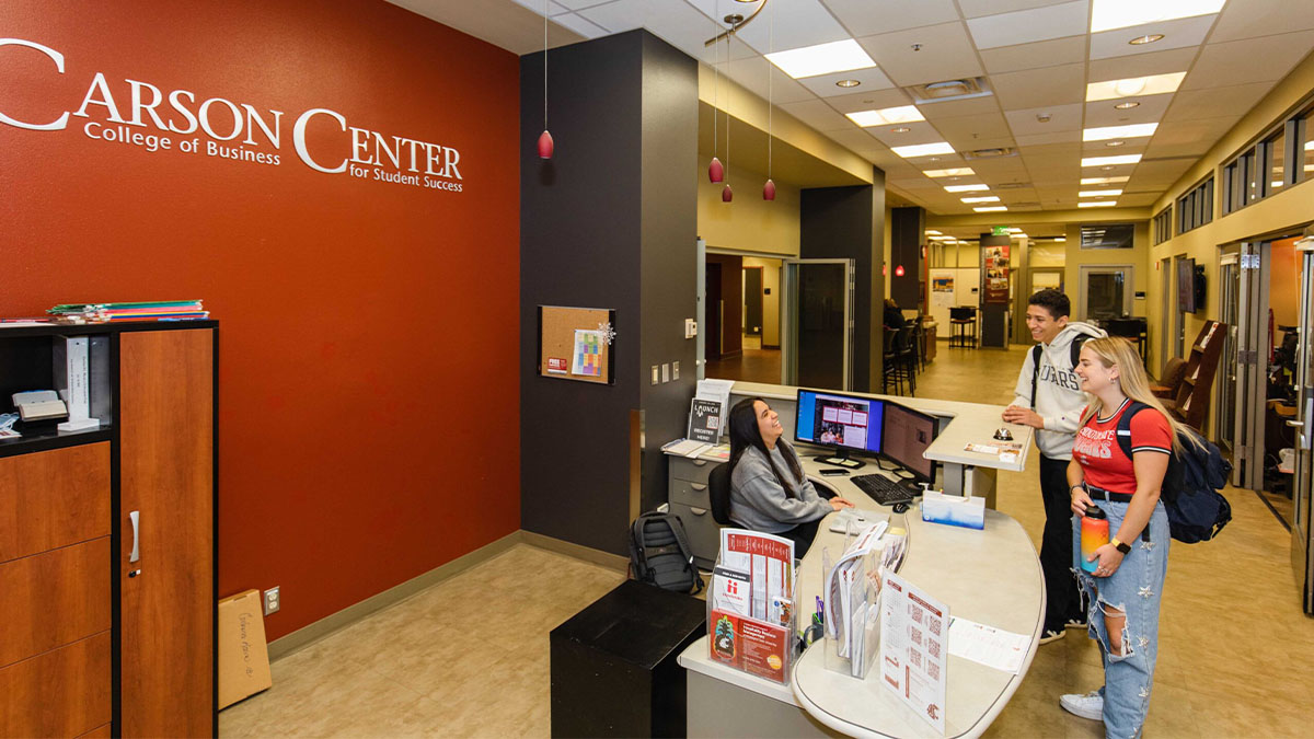 Students speak with a staff member at the Carson Center reception desk beneath Carson Center for Student Success signage.
