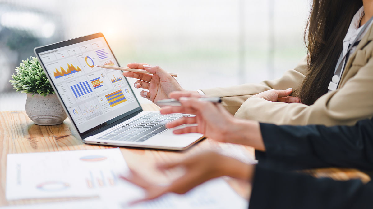 People review charts and financial data on a laptop during a business meeting, discussing analysis and performance metrics.