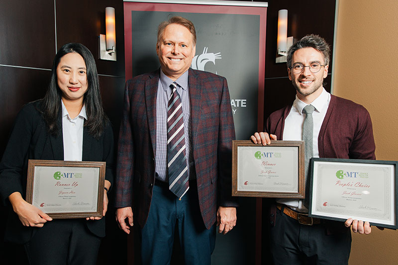 Three people holding certificates in front of a WSU banner. Jiyoon Han holds “Runner Up,” Chuck Munson stands in the middle, and Josh Groves holds “Winner” and “People’s Choice.