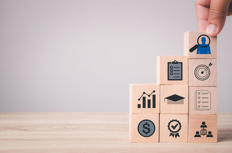 Hand placing a wooden block with icons representing goals, teamwork, and achievement.