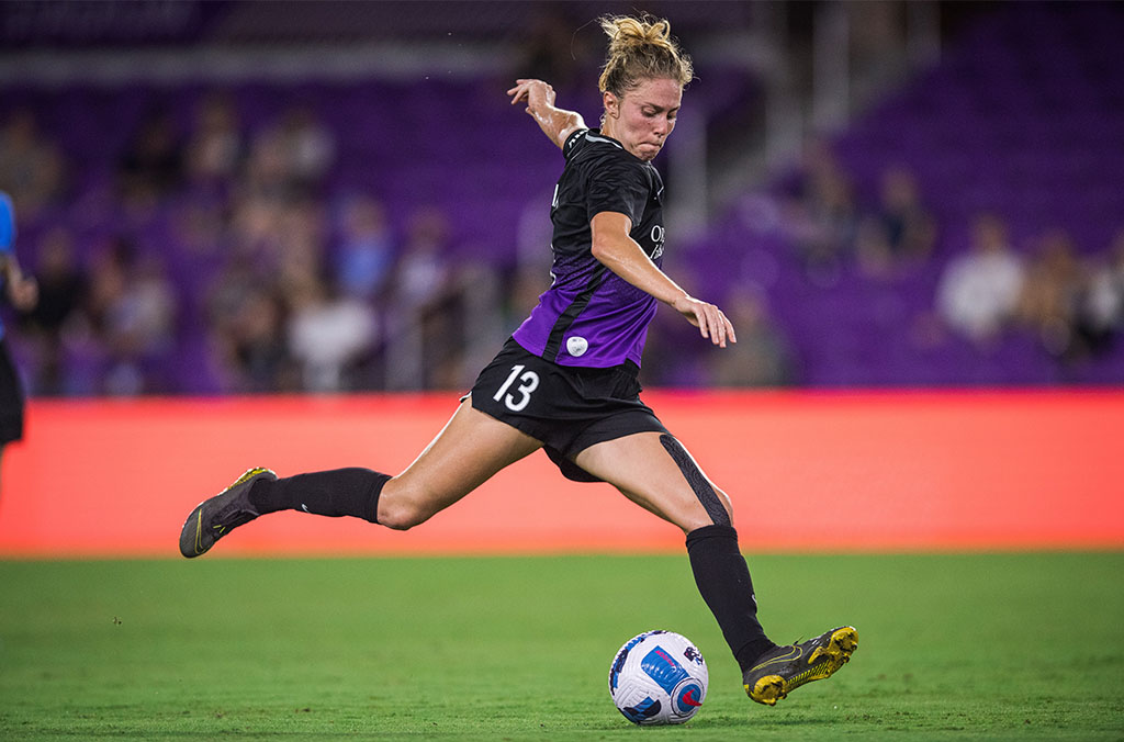 Celia Jimenez Delgado in a black and purple uniform, mid-stride about to kick a soccer ball.