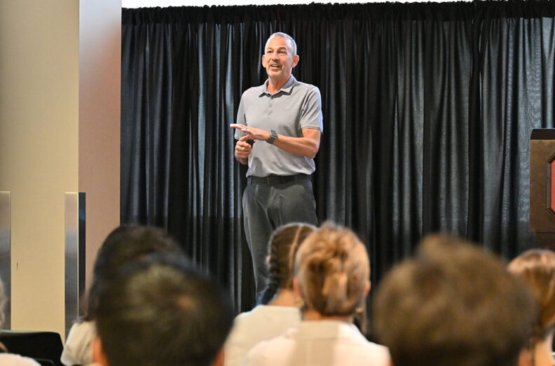 Joe Valacich speaking during the Hubman Lecture, standing in front of a black curtain with an audience seated in the foreground.