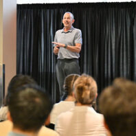 Joe Valacich speaking during the Hubman Lecture, standing in front of a black curtain with an audience seated in the foreground.