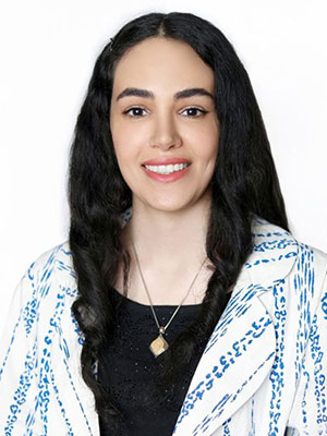Mahsa Zohrabi wearing a patterned white and blue top with long dark hair, photographed against a plain white background.