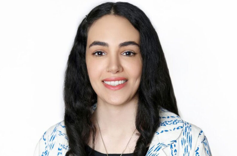 Mahsa Zohrabi wearing a patterned white and blue top with long dark hair, photographed against a plain white background.